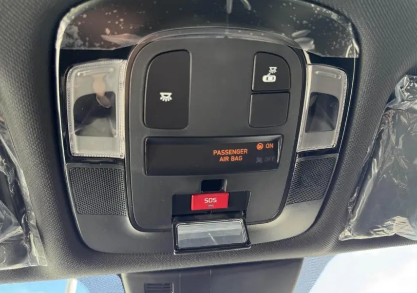Vue en gros plan du panneau de commandes au plafond du Hyundai Tucson noir avec bouton SOS et indicateur airbag passager.