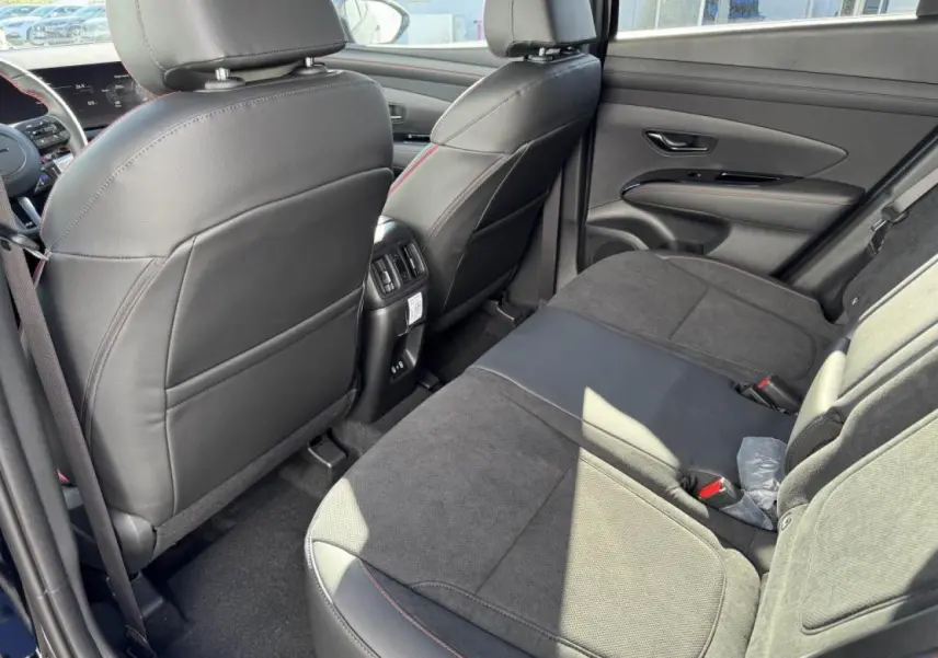 Vue arrière intérieure du Hyundai Tucson 2025, sièges cuir/alcantara noirs avec surpiqûres rouges et accoudoir central.