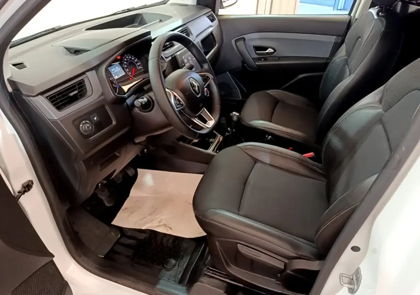 Vue intérieure côté conducteur de la Renault Express Confort blanche, montrant le tableau de bord et les sièges noirs.