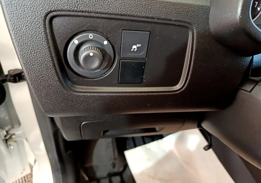 Gros plan sur les commandes de réglage des phares et antipatinage à gauche du volant d’un Renault Express blanc.