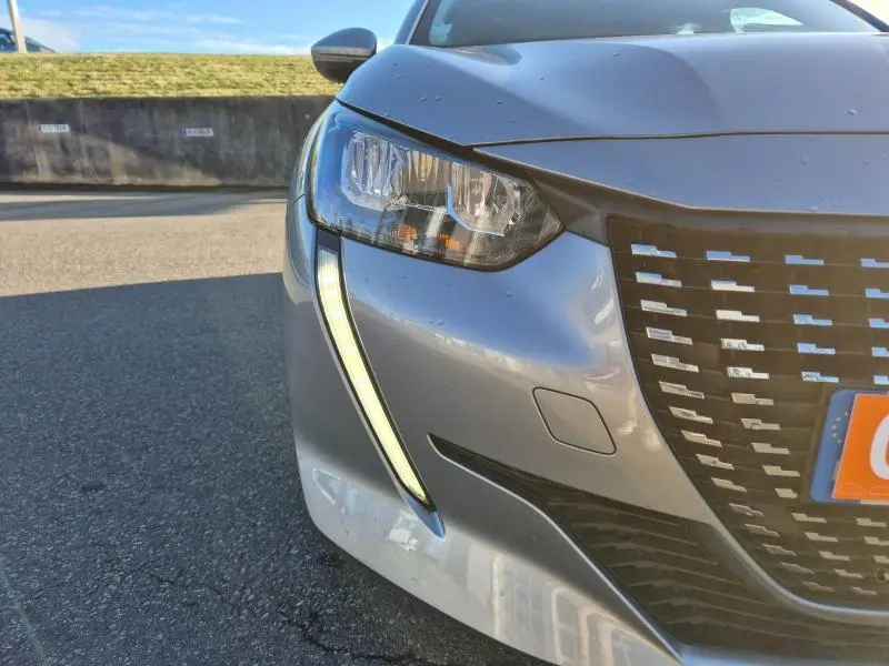Gros plan sur l'avant droit d'une Peugeot 208 gris Artense avec feux LED et calandre au design moderne.