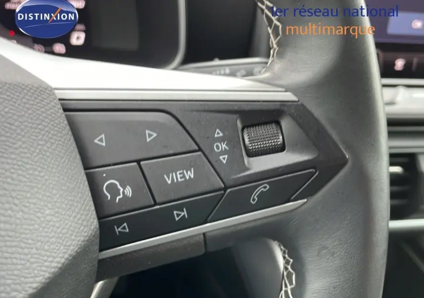 Gros plan sur les commandes gauche du volant en cuir noir du SEAT Leon bleu Fjord, avec boutons multifonctions visibles.