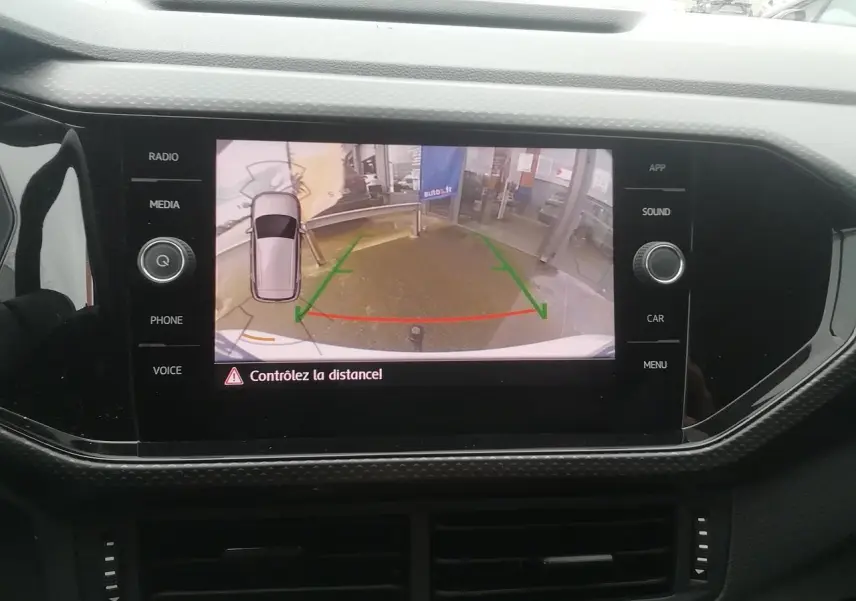Écran tactile intérieur montrant la caméra de recul du Volkswagen T-Cross blanc, avec repères de guidage colorés.
