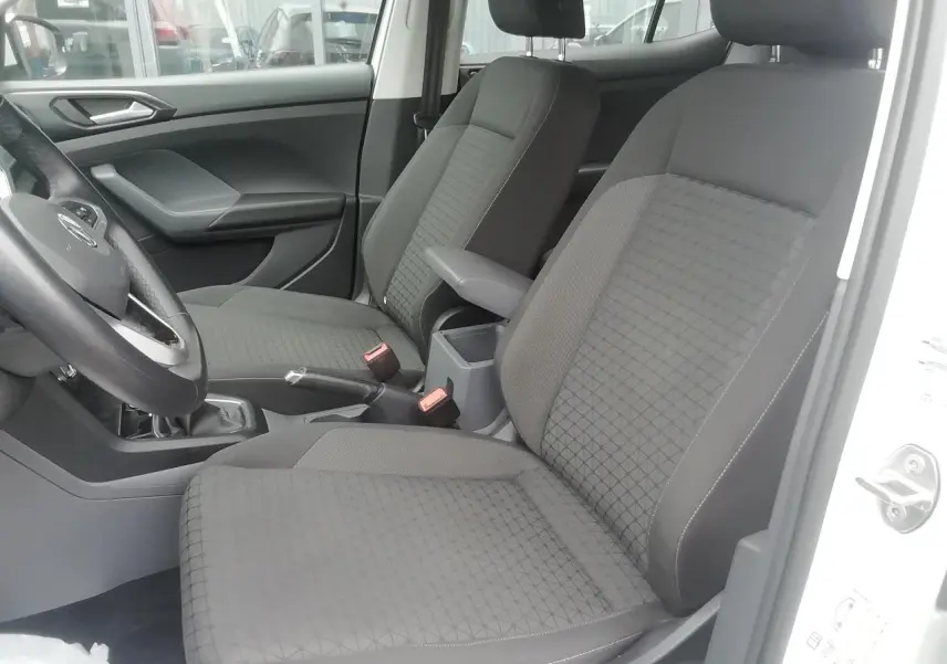 Vue intérieure côté gauche du Volkswagen T-Cross blanc 2020, montrant les sièges avant en tissu gris et l'accoudoir central.