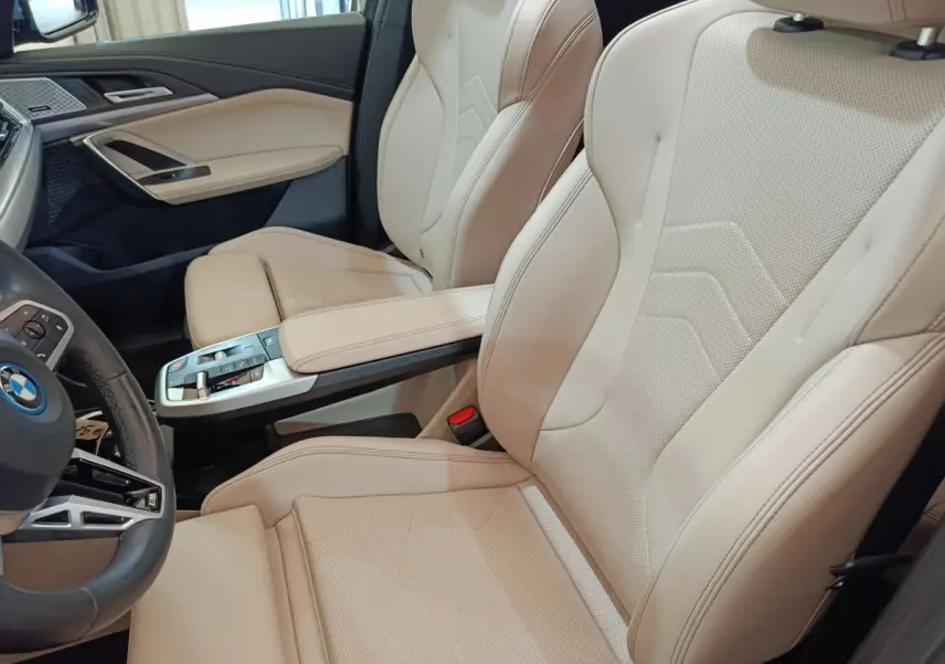 Vue intérieure côté conducteur du BMW X1 xDrive25e 2024, sièges cuir beige et console centrale moderne.