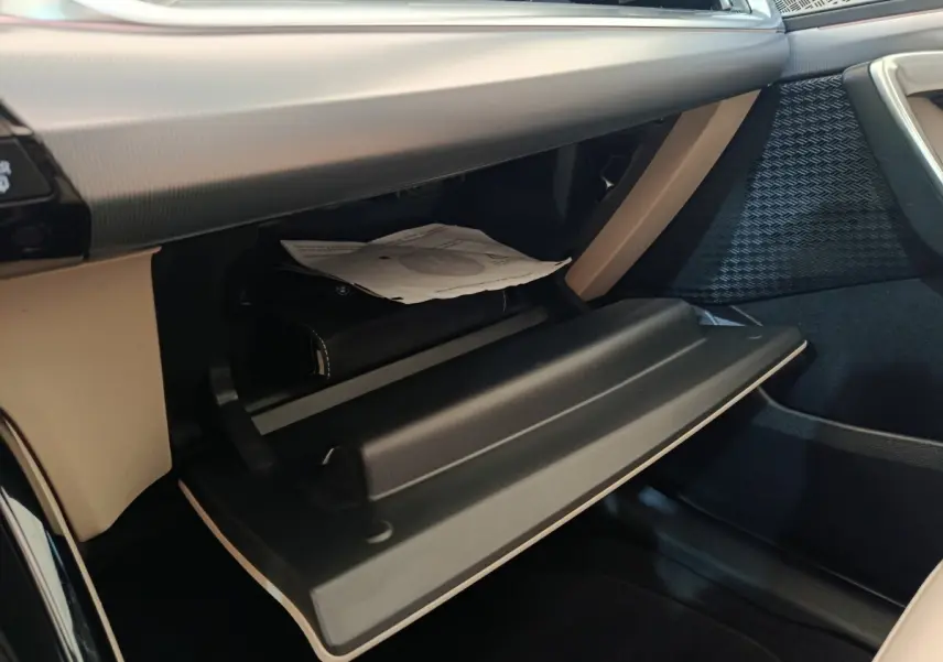 Gros plan sur la boîte à gants ouverte de la BMW X1 xDrive25e M Sport 2024, intérieur beige et noir.