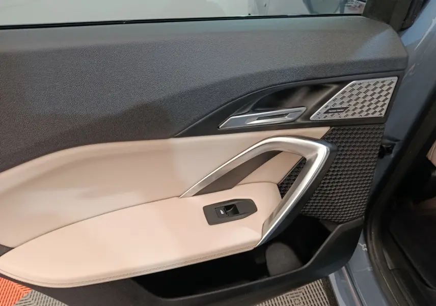 Gros plan sur la porte avant gauche gris foncé du BMW X1 xDrive25e M Sport avec garniture beige et haut-parleur Harman Kardon.