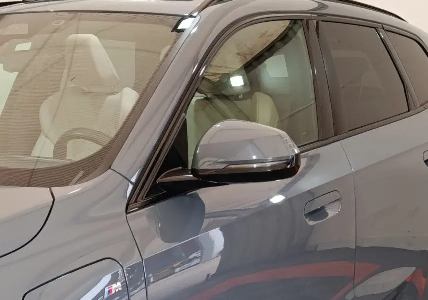 Vue rapprochée côté gauche d’un BMW X1 xDrive25e M Sport gris foncé avec rétroviseur et badge M Sport visibles.
