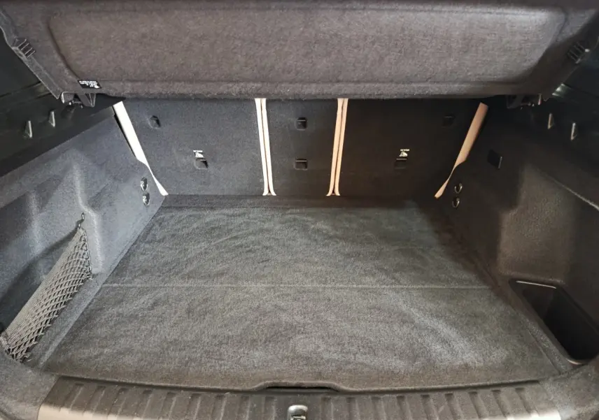 Coffre spacieux ouvert de BMW X1 xDrive25e M Sport gris foncé, avec tapis et filet de rangement latéral visible.