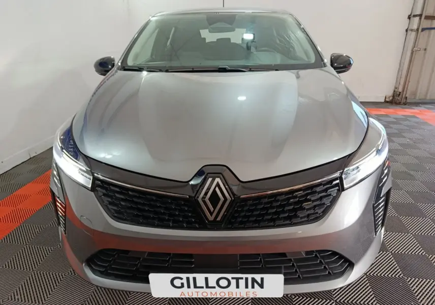 Vue frontale d'une Renault Clio gris foncé avec calandre noire et phares LED allumés dans un garage.