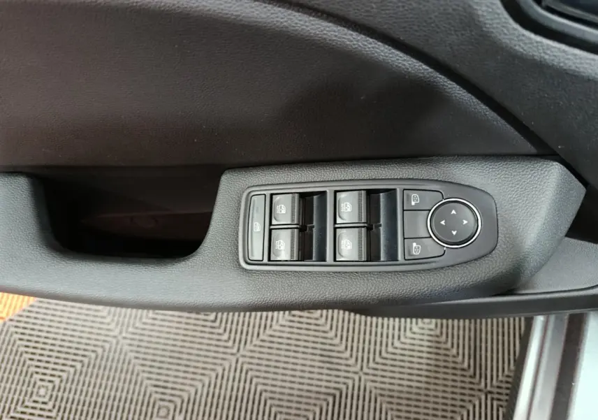 Gros plan sur les commandes des vitres électriques et rétroviseurs côté conducteur d'une Renault Clio gris foncé 2025.