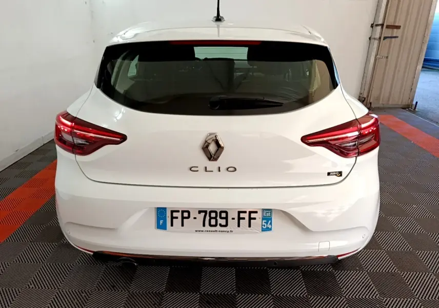 Vue arrière d'une Renault Clio blanche 2020 avec feux LED et logo centré sur un sol à damiers noir et orange.