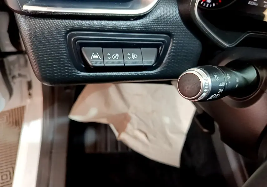 Gros plan sur les commandes d'assistance à la conduite et réglage des phares à gauche du volant dans une Renault Clio blanche 2020.