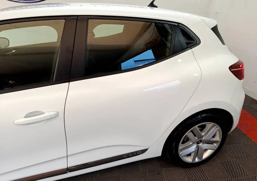 Vue latérale droite d'une Renault Clio blanche avec jante alliage et logo Clio sur la bas de porte.