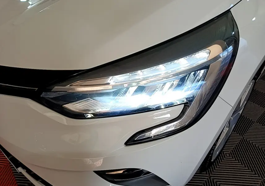 Gros plan sur le phare avant droit allumé d'une Renault Clio Business Blue dCi 115 blanche de 2020.