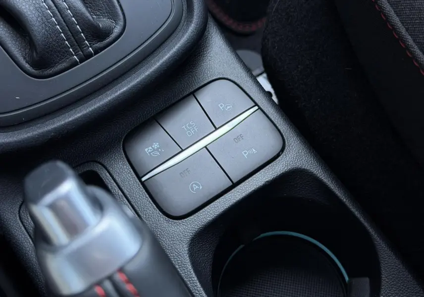 Gros plan sur les commandes du pack sécurité et stationnement dans la console centrale noire du Ford Puma rouge.