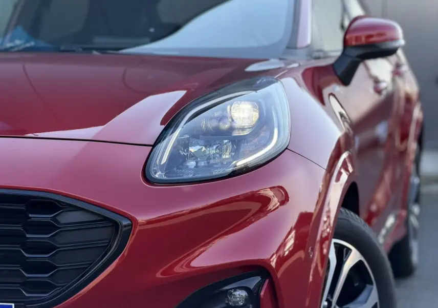Gros plan sur l’avant droit du Ford Puma rouge Fantastic, mettant en valeur le phare LED et la calandre noire hexagonale.