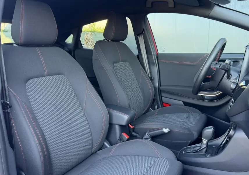 Vue intérieure côté conducteur du Ford Puma rouge, montrant les sièges noirs avec surpiqûres rouges et volant ST-Line.
