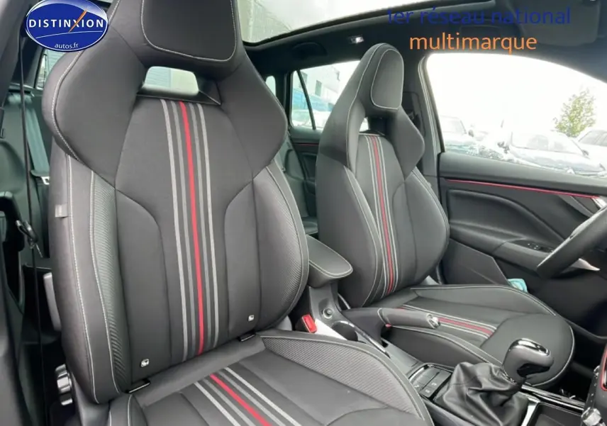 Vue intérieure avant du Skoda Kamiq noir 2026, sièges sport noirs avec bandes rouges et grises, volant cuir multifonction.
