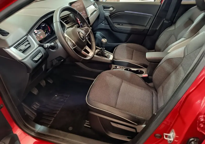 Intérieur côté conducteur du Renault Captur Techno TCe 90 rouge 2024, volant multifonctions et levier de vitesse manuel visibles.