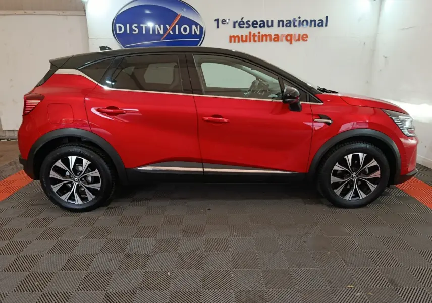 Profil droit d'un Renault Captur rouge 2024 avec jantes alliage et toit noir dans un showroom intérieur.