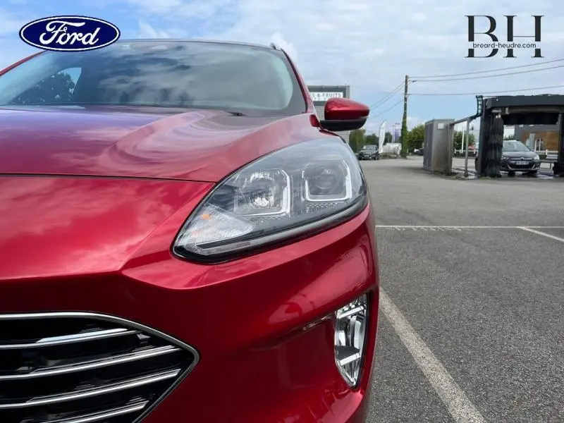 Gros plan sur l'avant droit du Ford Kuga 2022 rouge Premium Lucid, mettant en valeur le phare et la calandre chromée.