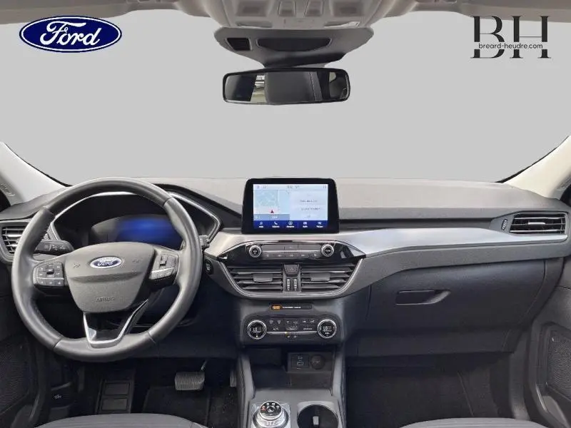 Vue intérieure avant du Ford Kuga 2022 avec tableau de bord noir, écran tactile central et volant cuir multifonction.