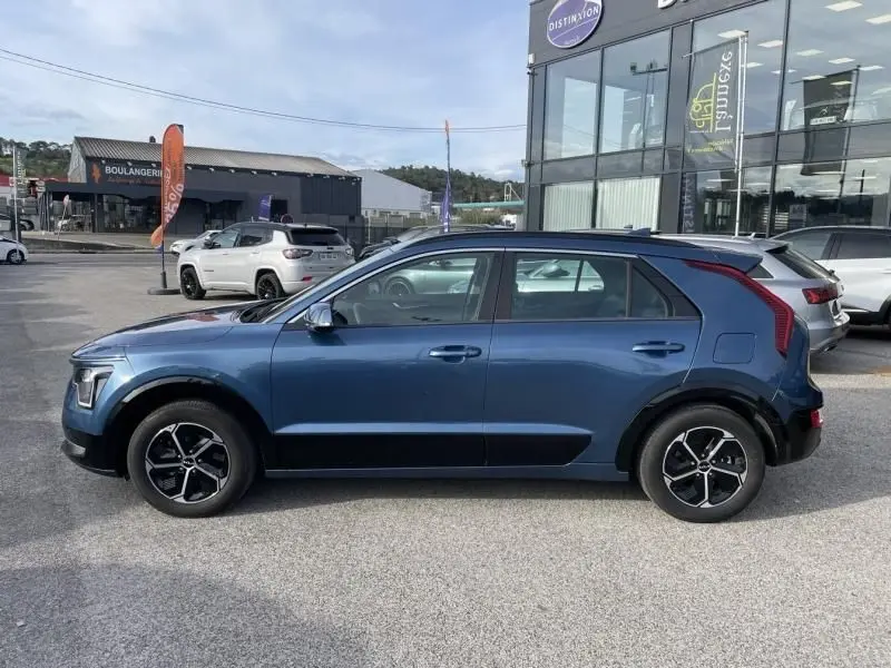 Vue de profil côté gauche d'un KIA NIRO 2024 bleu métal avec jantes noires et détails noirs sur les bas de caisse.