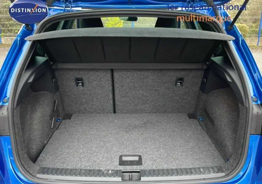 Coffre ouvert vu de l'arrière d'un SEAT Arona bleu saphir métal avec intérieur de coffre gris et cache-bagages relevé.