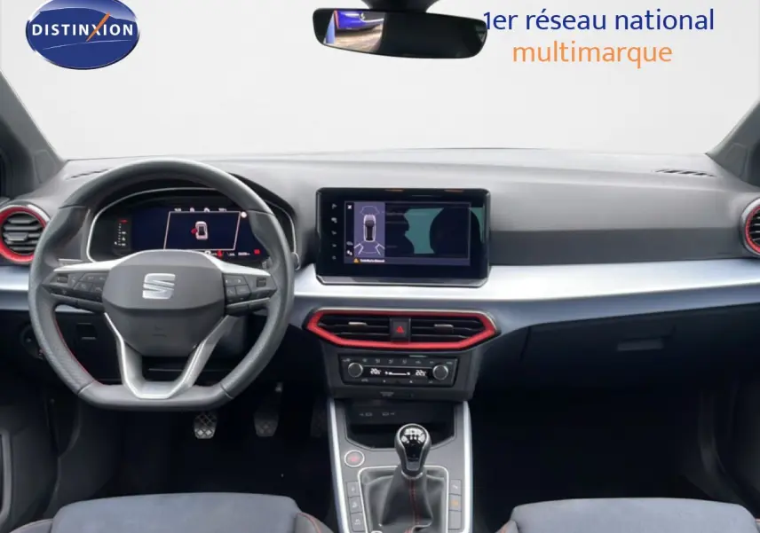 Vue intérieure frontale du tableau de bord de la SEAT Arona 2025, volant cuir noir et détails rouges autour des aérateurs.