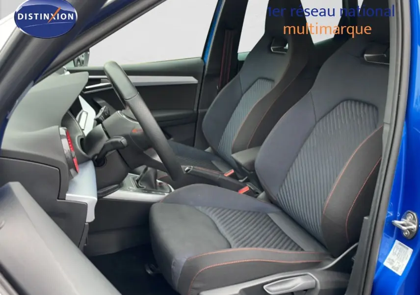 Vue intérieure côté conducteur du SEAT Arona bleu saphir avec sièges sport noirs à surpiqûres orange.