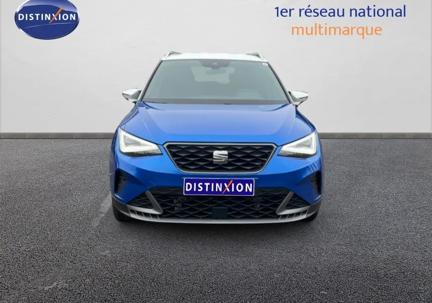 Vue frontale d'un SEAT Arona bleu saphir métal avec toit blanc, calandre noire et phares LED allumés.
