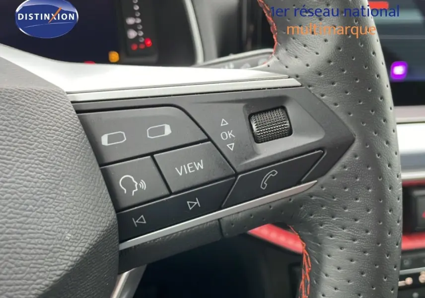 Gros plan sur les commandes multifonctions du volant en cuir perforé noir avec surpiqûres rouges du SEAT Arona bleu saphir.