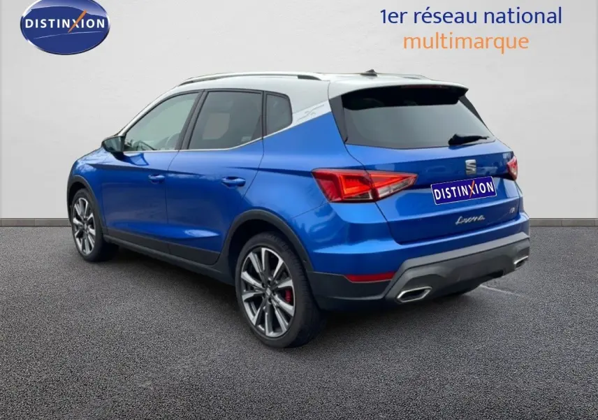 SEAT Arona 2025 bleu saphir métal avec toit blanc, vue 3/4 arrière côté gauche, jantes alliage et feux LED.