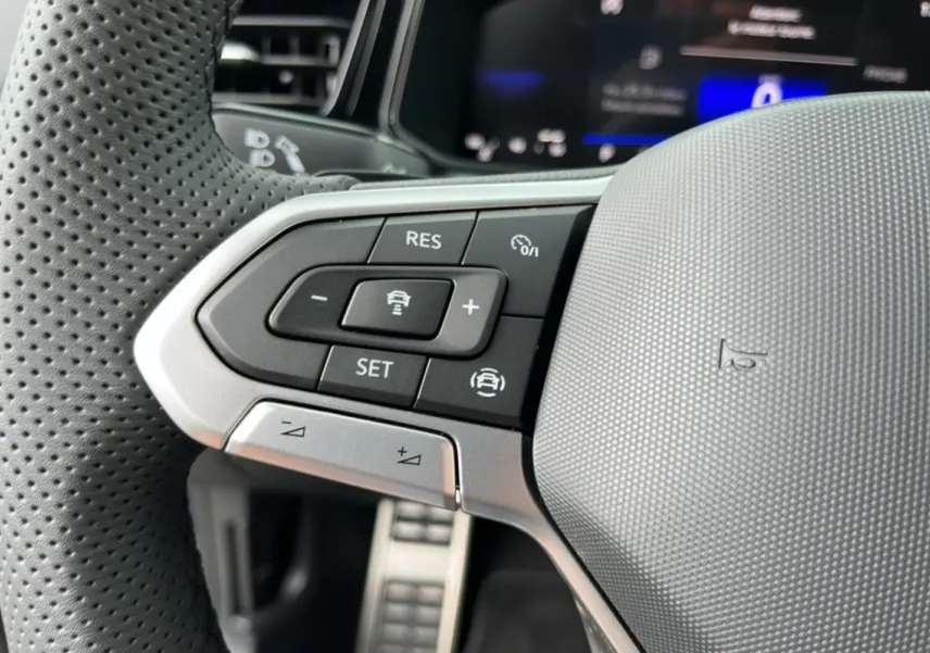 Gros plan sur les commandes de régulateur de vitesse au volant cuir perforé du Volkswagen T-Roc TDI 150 R-Line noir.