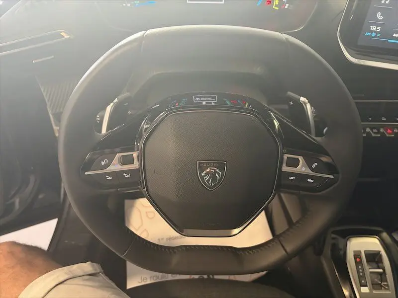 Vue rapprochée du volant noir du Peugeot 2008 Hybrid 145ch, avec commandes intégrées et tableau de bord partiellement visible.