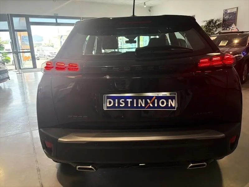 Vue arrière d’un Peugeot 2008 noir métal hybride, avec feux LED allumés et plaque Distinxion en concession.