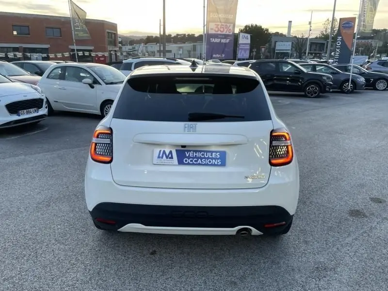 Vue arrière d'une FIAT 600 blanche 1.2 Hybrid La Prima 2025 avec feux arrière allumés sur parking de véhicules d'occasion.