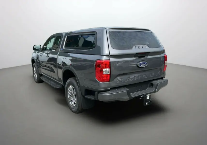 Ford Ranger gris carbone en 3/4 arrière droit avec hard-top vitré et attelage visible.