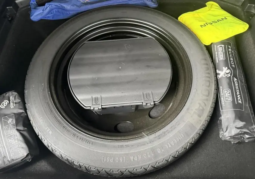 Vue rapprochée de la roue de secours galette dans le coffre d'un Peugeot 3008 blanc avec kit d'assistance et trousse de secours.