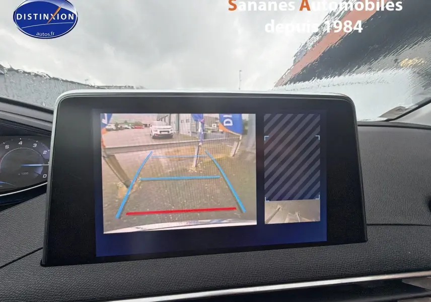 Écran tactile intérieur montrant la caméra de recul d'un Peugeot 3008 blanc, vue frontale sous la pluie.