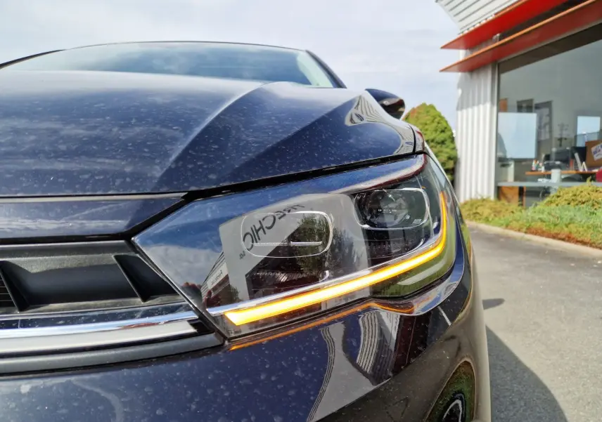 Gros plan sur le phare avant droit allumé d'une Volkswagen Polo noire 2022, avec reflets du bâtiment en arrière-plan.