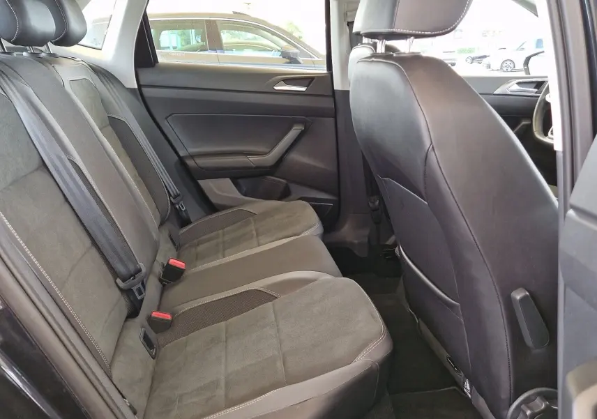 Vue intérieure arrière droite de la Volkswagen Polo noire 2022, sièges en tissu gris et cuir avec ceintures de sécurité visibles.