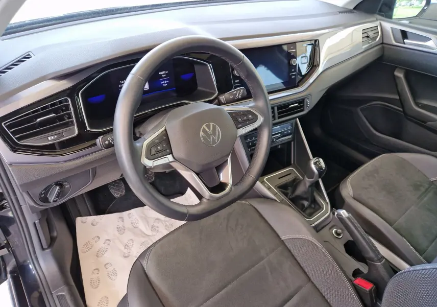 Vue intérieure côté conducteur d'une Volkswagen Polo noire 2022, volant multifonction et levier de vitesse manuel visibles.