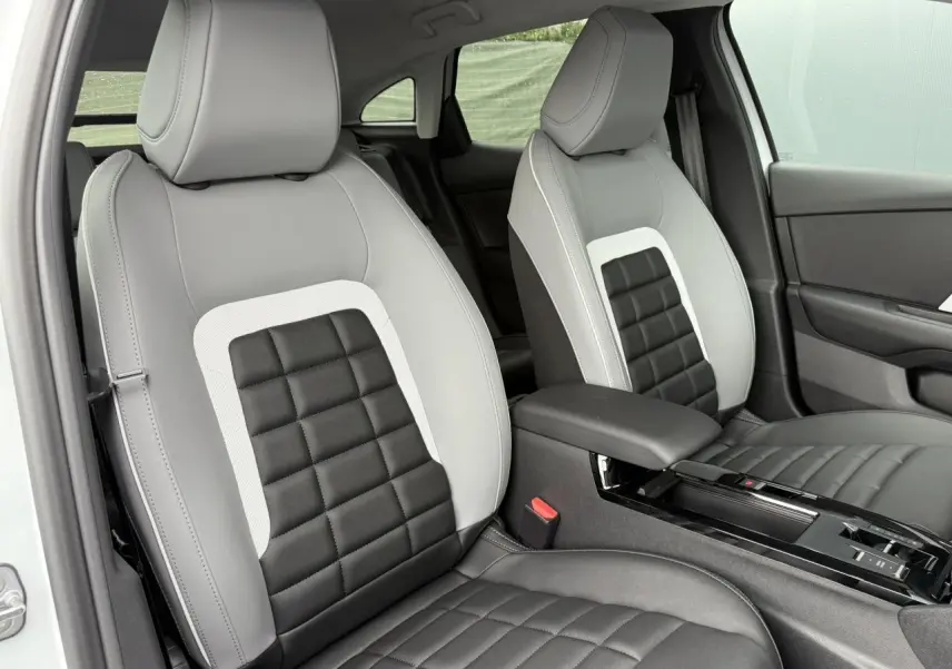 Vue rapprochée des sièges avant gris clair et noir matelassé de la Citroën C4 NV Hybrid 2025, avec accoudoir central.