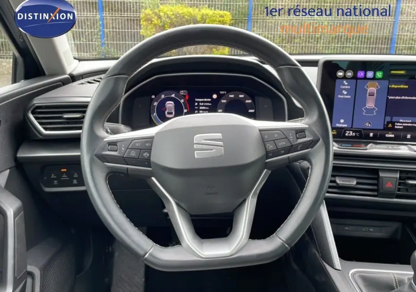 Vue intérieure centrée sur le volant cuir multifonction de la SEAT LEON ST 2025 avec tableau de bord digital et écran tactile.