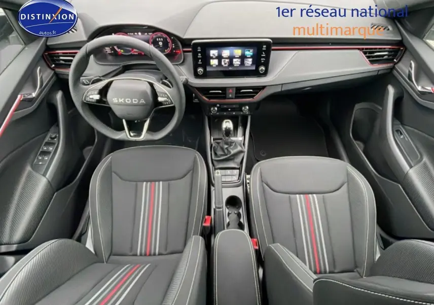 Vue intérieure avant du Skoda Kamiq blanc nacré 2026, avec tableau de bord moderne et sièges sport noirs à bandes rouges.