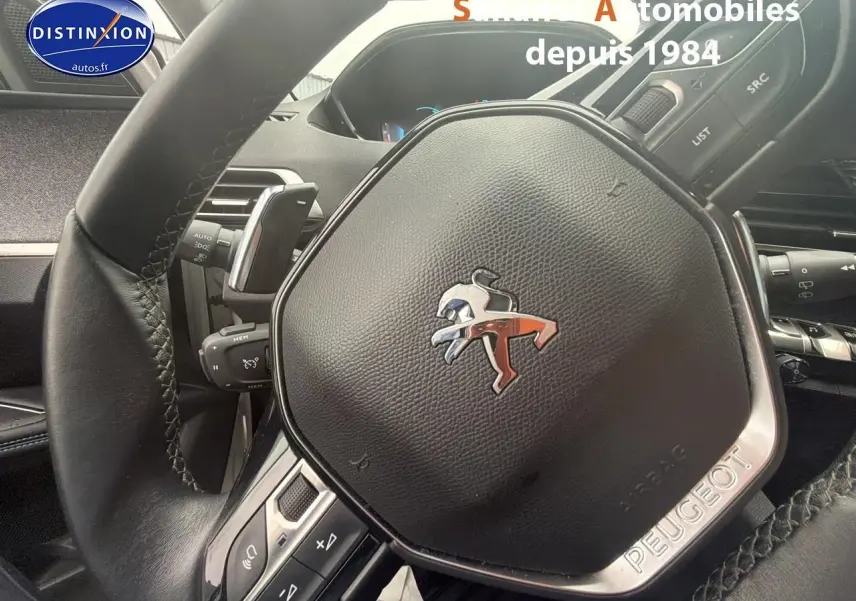 Gros plan sur le volant cuir noir du Peugeot 3008 Hybrid 2021 avec logo lion chromé et commandes intégrées.