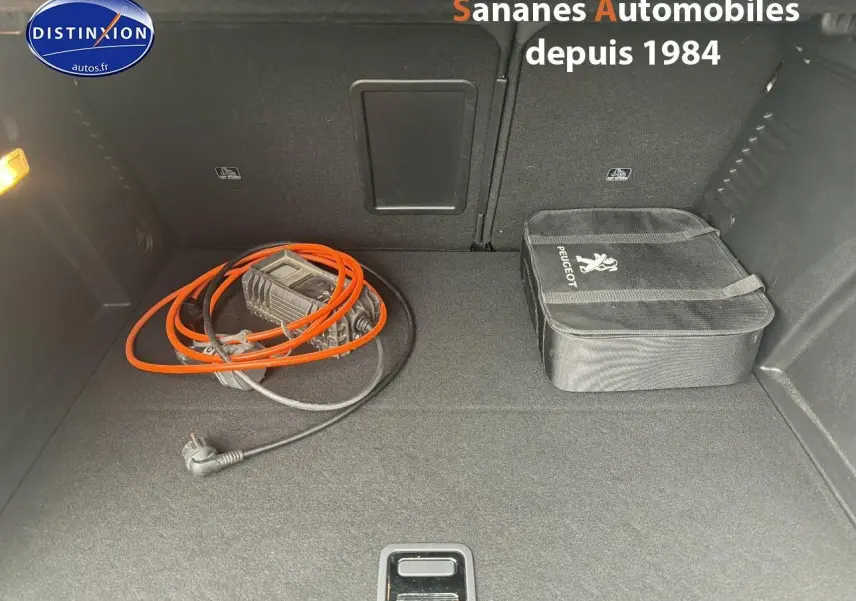 Coffre ouvert d’un Peugeot 3008 Hybrid blanc, vue plongeante montrant câble de recharge et sacoche Peugeot.