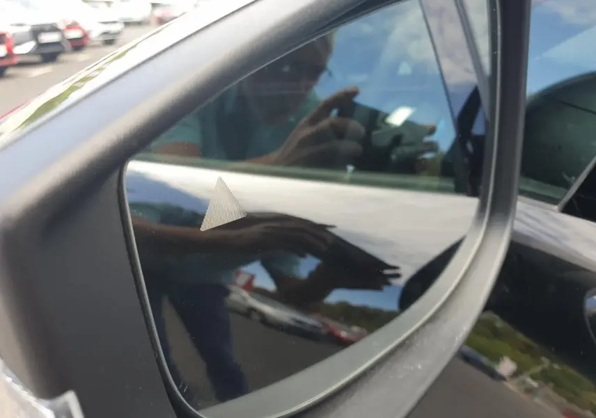 Rétroviseur côté gauche d’une Renault Clio VI noire étoile, reflétant partiellement l’environnement extérieur.